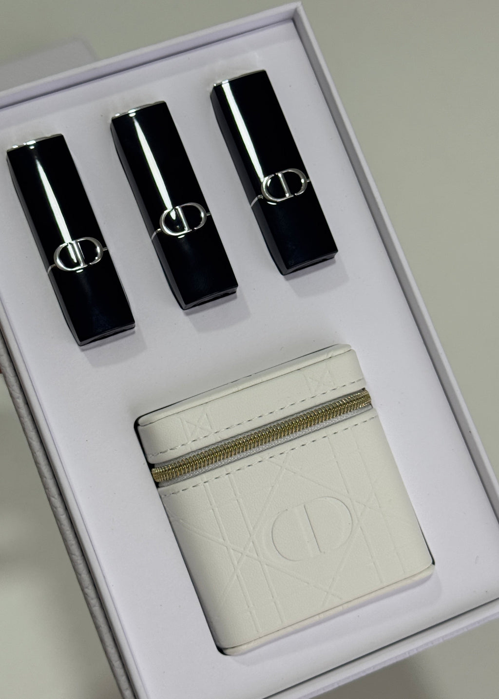 A Dior gift set in a white box containing three black lipsticks with silver trim and a white leather pouch with an embossed Dior logo.