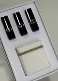 A Dior gift set in a white box containing three black lipsticks with silver trim and a white leather pouch with an embossed Dior logo.