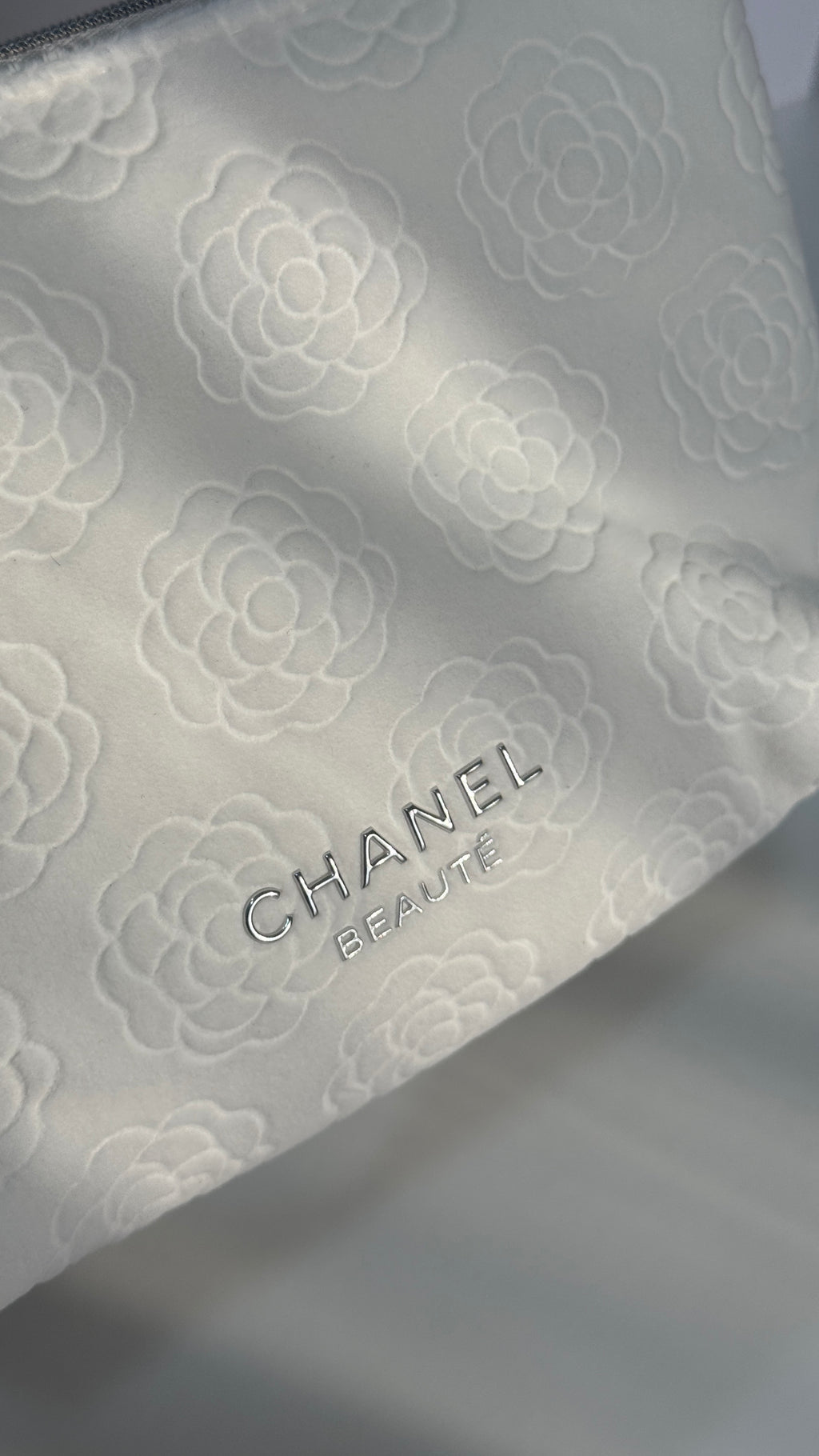 Close-up of a white Chanel beauty pouch with an embossed floral pattern and the CHANEL BEAUTY logo.