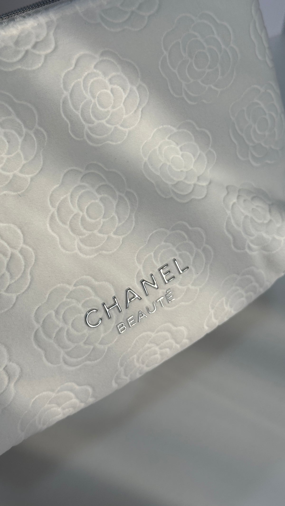 Close-up of a white Chanel beauty pouch with an embossed floral pattern and the CHANEL BEAUTY logo.