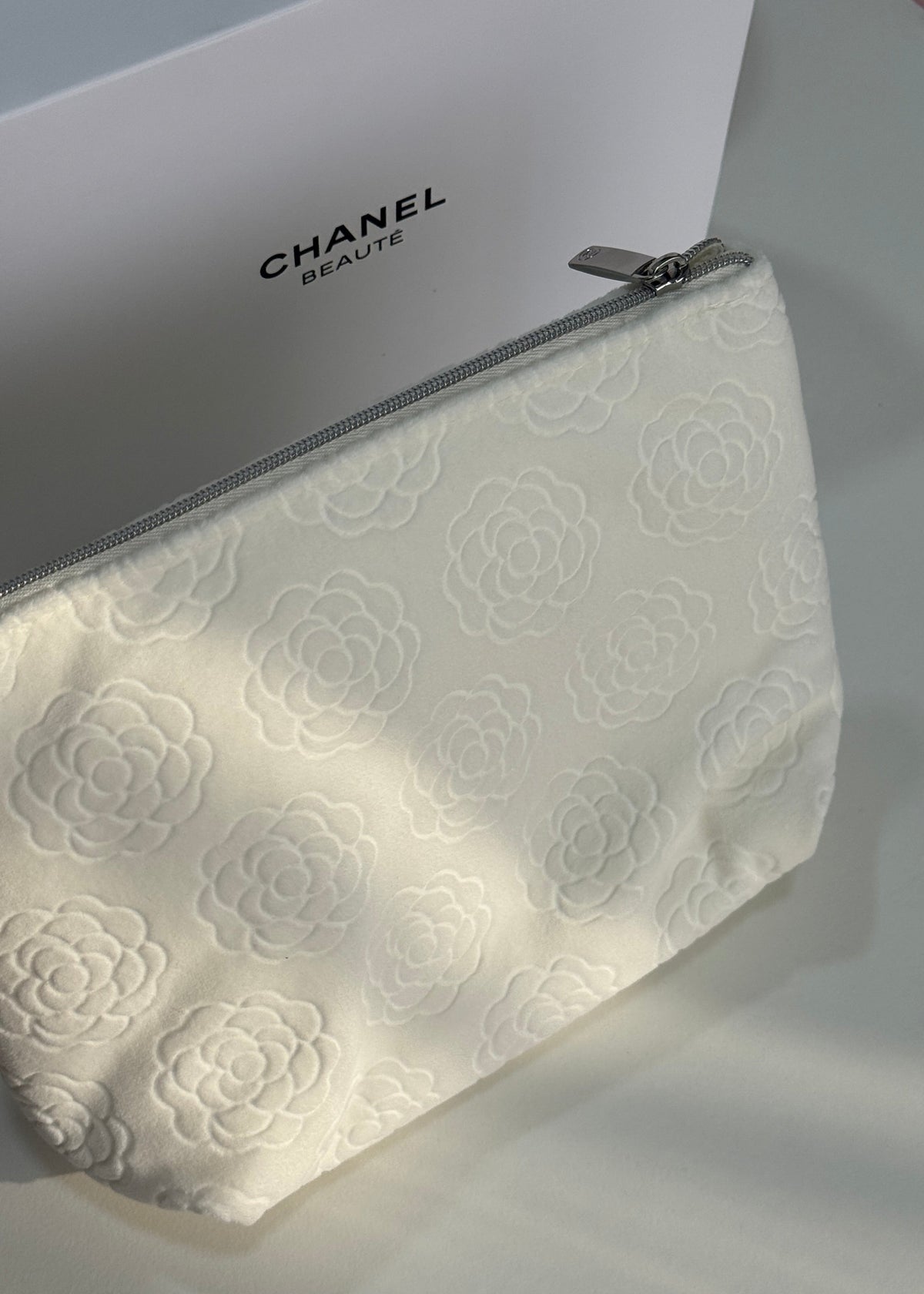 A Chanel cosmetic pouch in off-white jacquard fabric with a tonal camellia pattern, shown next to its white Chanel box.