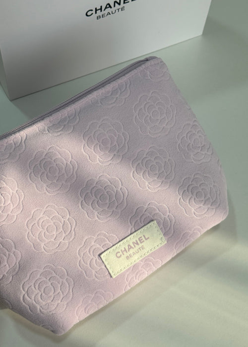 A Chanel Beauté cosmetic pouch in light pink with a tonal embossed floral pattern and a cream-colored logo patch, shown next to its white Chanel box.