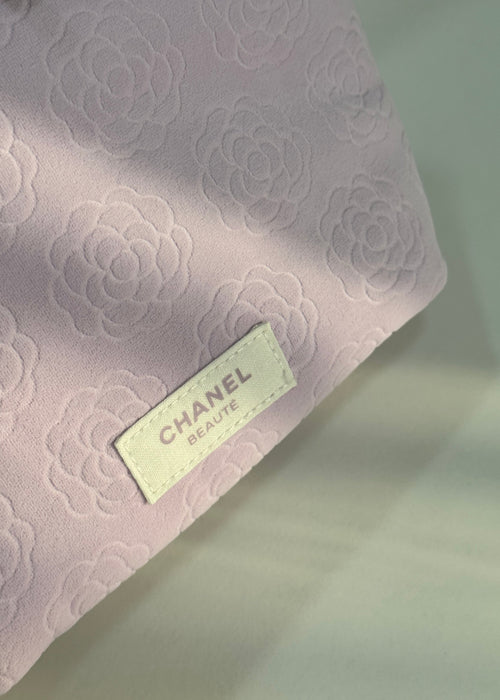 A close-up of a light pink Chanel Beauty pouch with an embossed floral pattern and a cream-colored brand label.