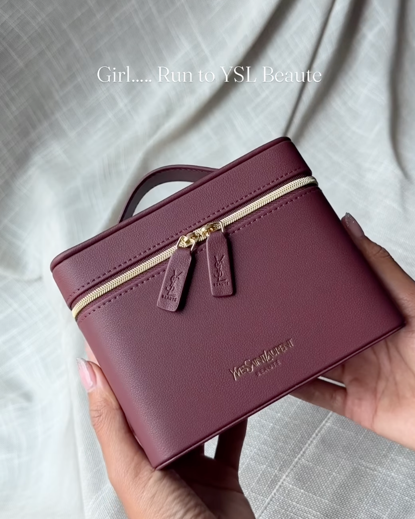 A burgundy faux leather cosmetic bag with gold zipper and hardware, held by two hands against a draped white fabric background.