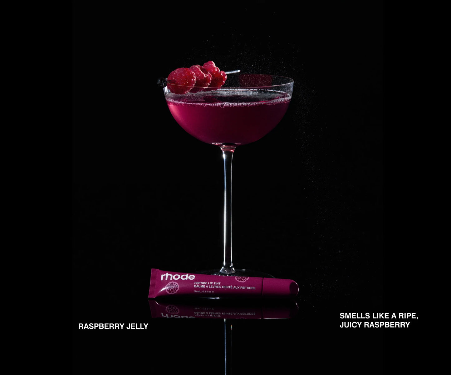 Purple cocktail in a glass with raspberries on a black background, featuring a Rhode product.